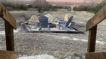 A wooden deck with two Adirondack chairs and a fire pit.