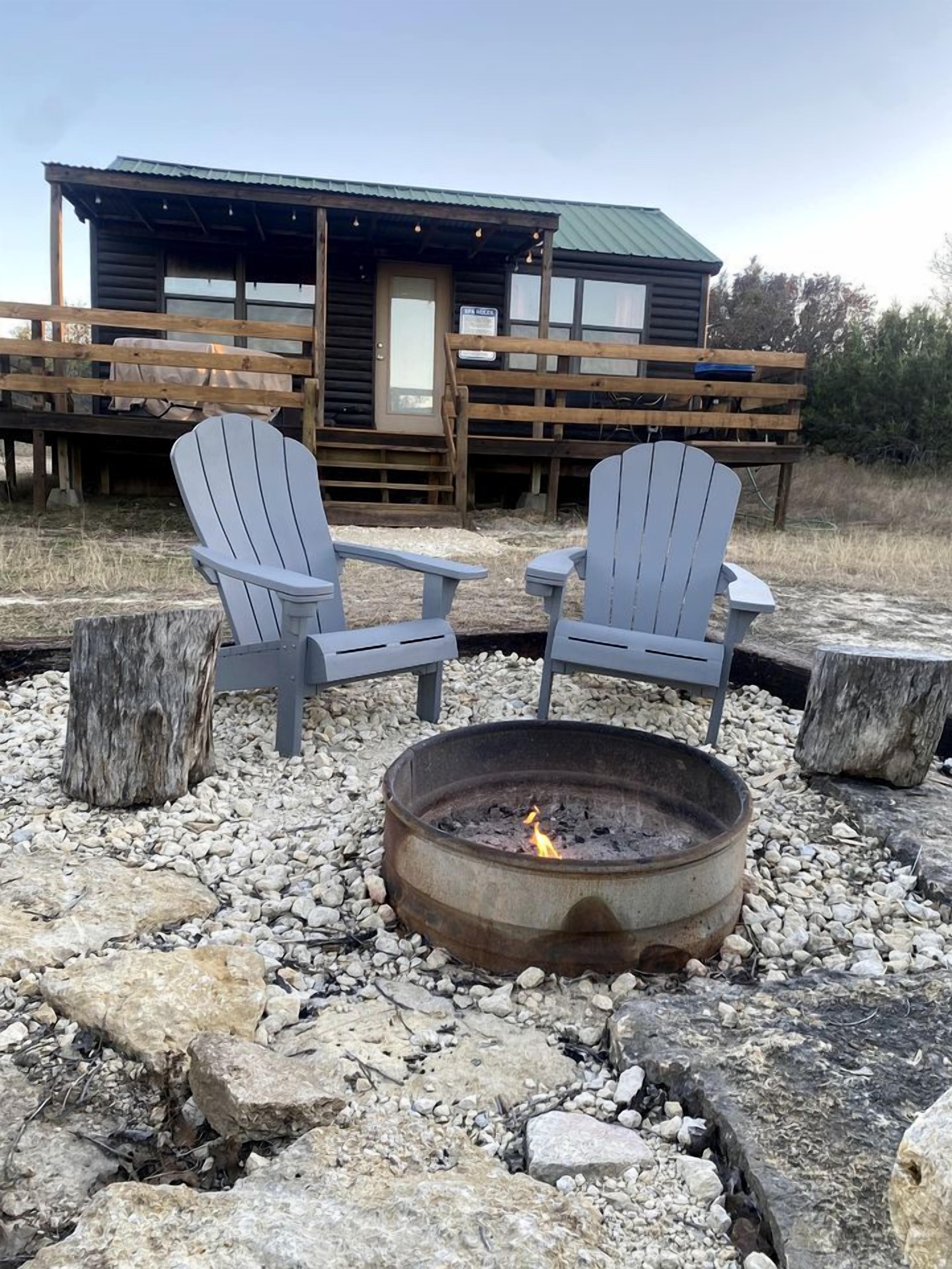 Eine rustikale Holzhütte mit zwei Adirondack-Stühlen rund um eine Feuerstelle.