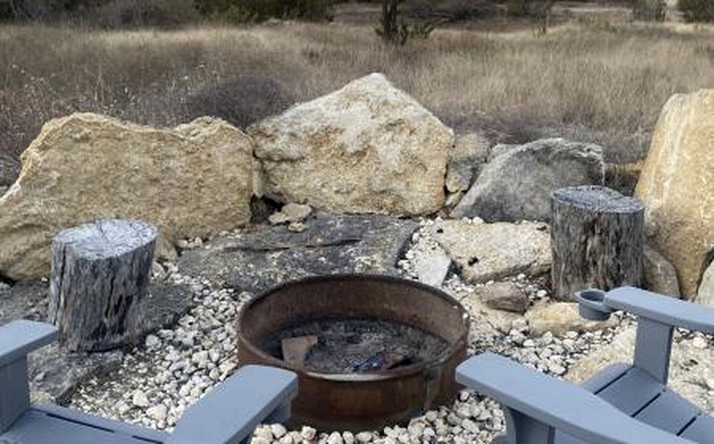Un foyer extérieur rustique, entouré de rochers et de poteaux en bois, offrant une vue dégagée sur le paysage environnant.