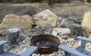 Un pozo de fuego rústico al aire libre rodeado de rocas y postes de madera, con una vista despejada del paisaje circundante.