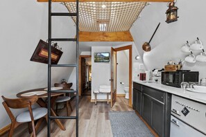 Een kleine keuken met een eethoek, houten meubels en uitzicht op de aangrenzende badkamer.