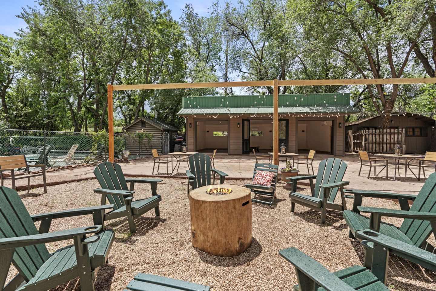 An outdoor seating area with Adirondack chairs, a wooden table, and a covered patio with string lights.