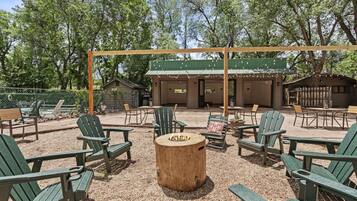 An outdoor seating area with Adirondack chairs, a wooden table, and a covered patio with string lights.