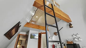 A loft-style room with a wooden ladder, a kitchen area with a microwave, and a white ceiling.