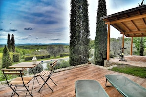 Una terraza de madera con mobiliario exterior, una pérgola y vistas al campo.