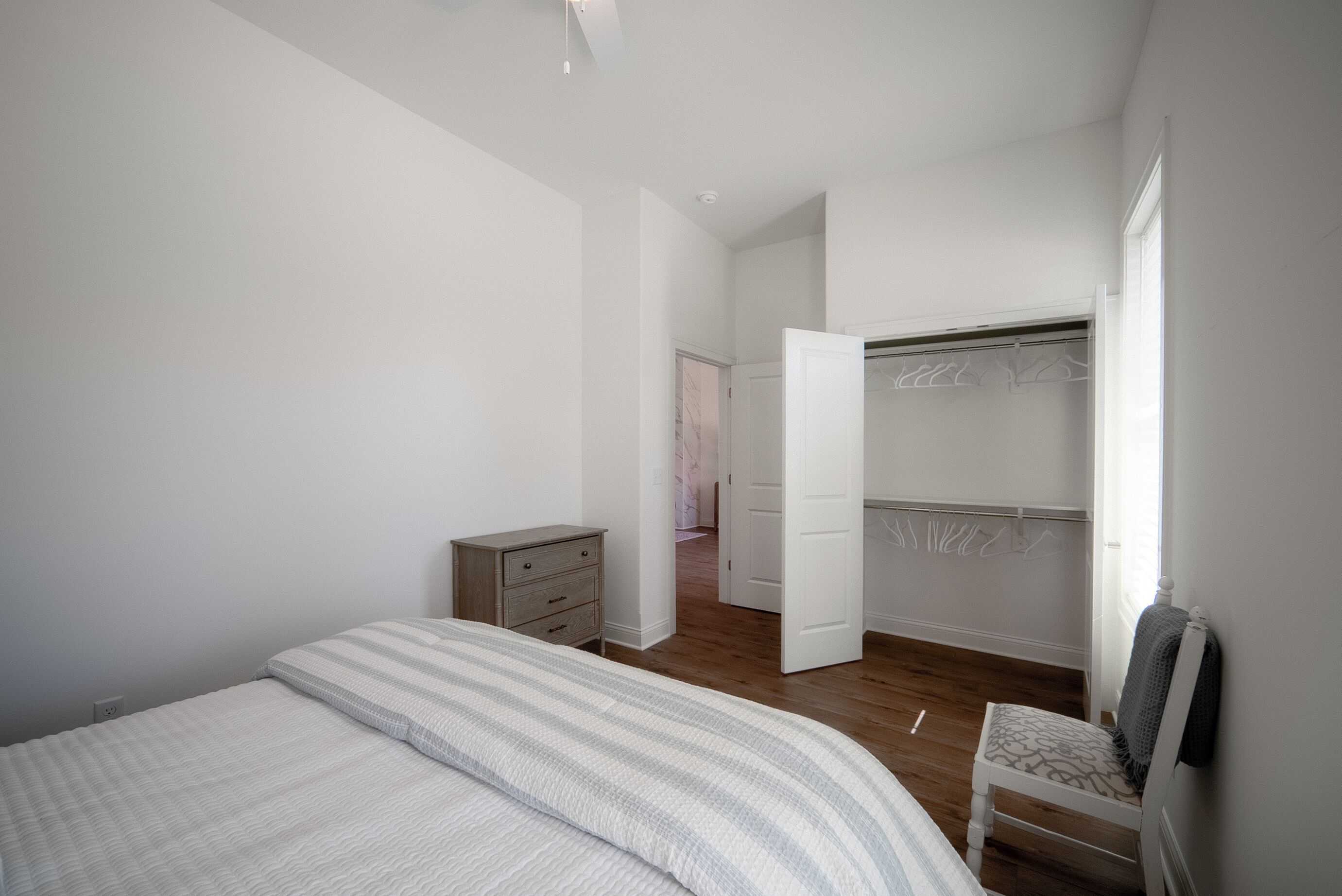 A bedroom with a bed, a dresser, a chair, and a walk-in closet.