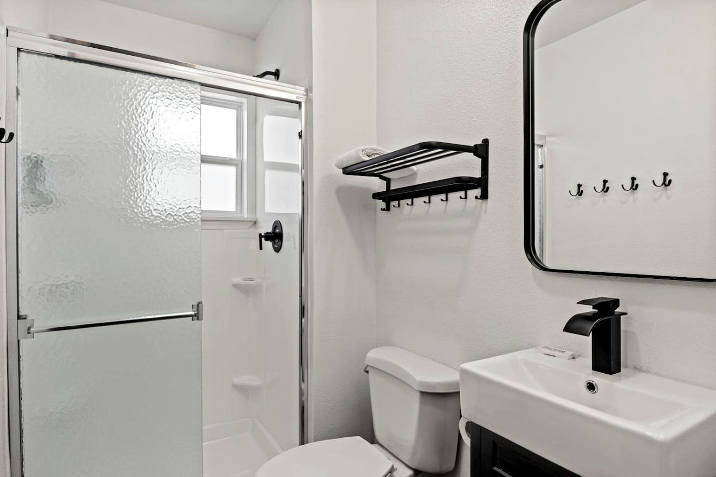 A bathroom with a white toilet, a sink with a black faucet, a towel rack, and a glass shower door.
