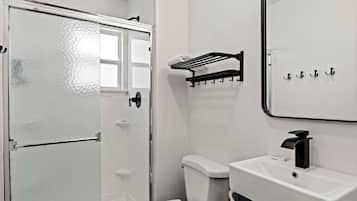 A bathroom with a white toilet, a sink with a black faucet, a towel rack, and a glass shower door.