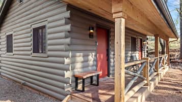A log cabin with a porch, a bench, and a red door.