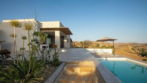 Una casa moderna con piscina, mobiliario exterior y vistas a las colinas.
