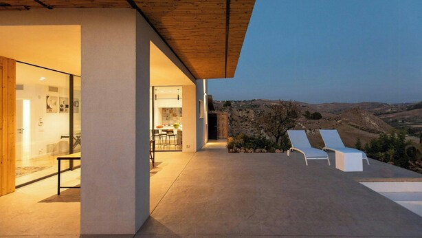 Una casa moderna con un patio, zona de comedor y vistas a las colinas.