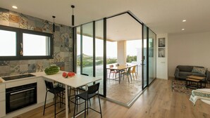 Una cocina moderna con un ventanal grande, un comedor con mesa y sillas, y una sala de estar con sofá y vistas al exterior.