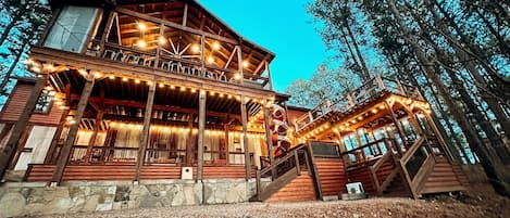 A wooden cabin with a balcony, stone foundation, and a staircase leading to the upper level.
