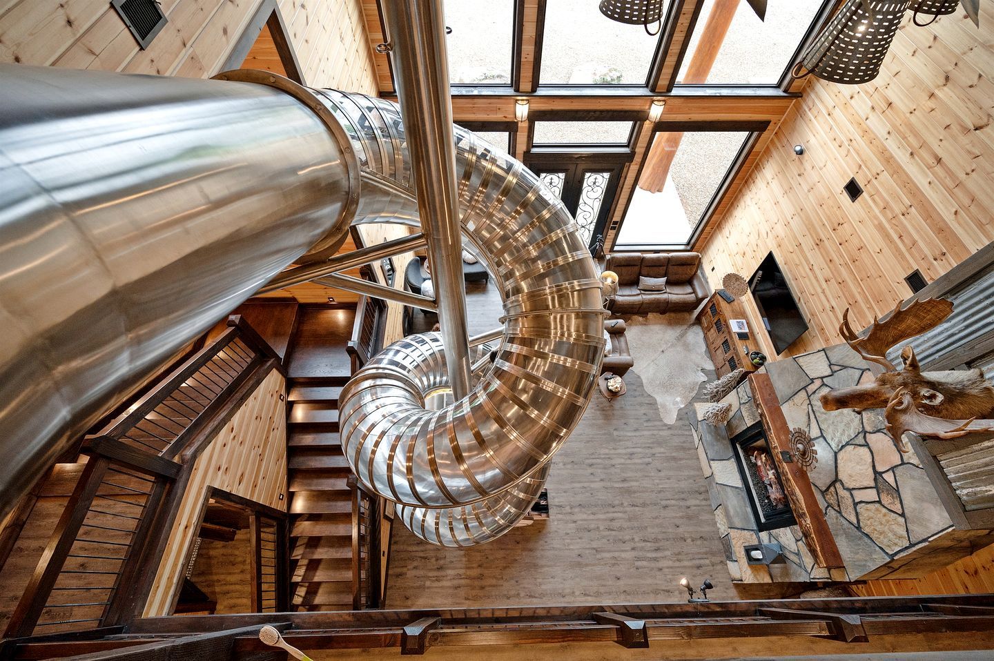 A spiral staircase with a metallic structure, wooden walls, and a stone fireplace.
