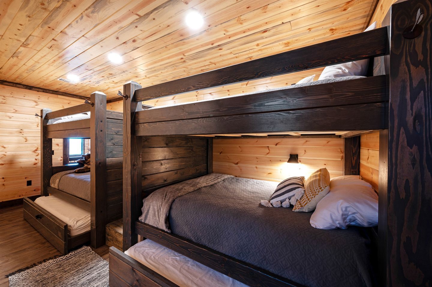 Quarto com beliche, paredes e teto de madeira, luminária de cabeceira e tapete.