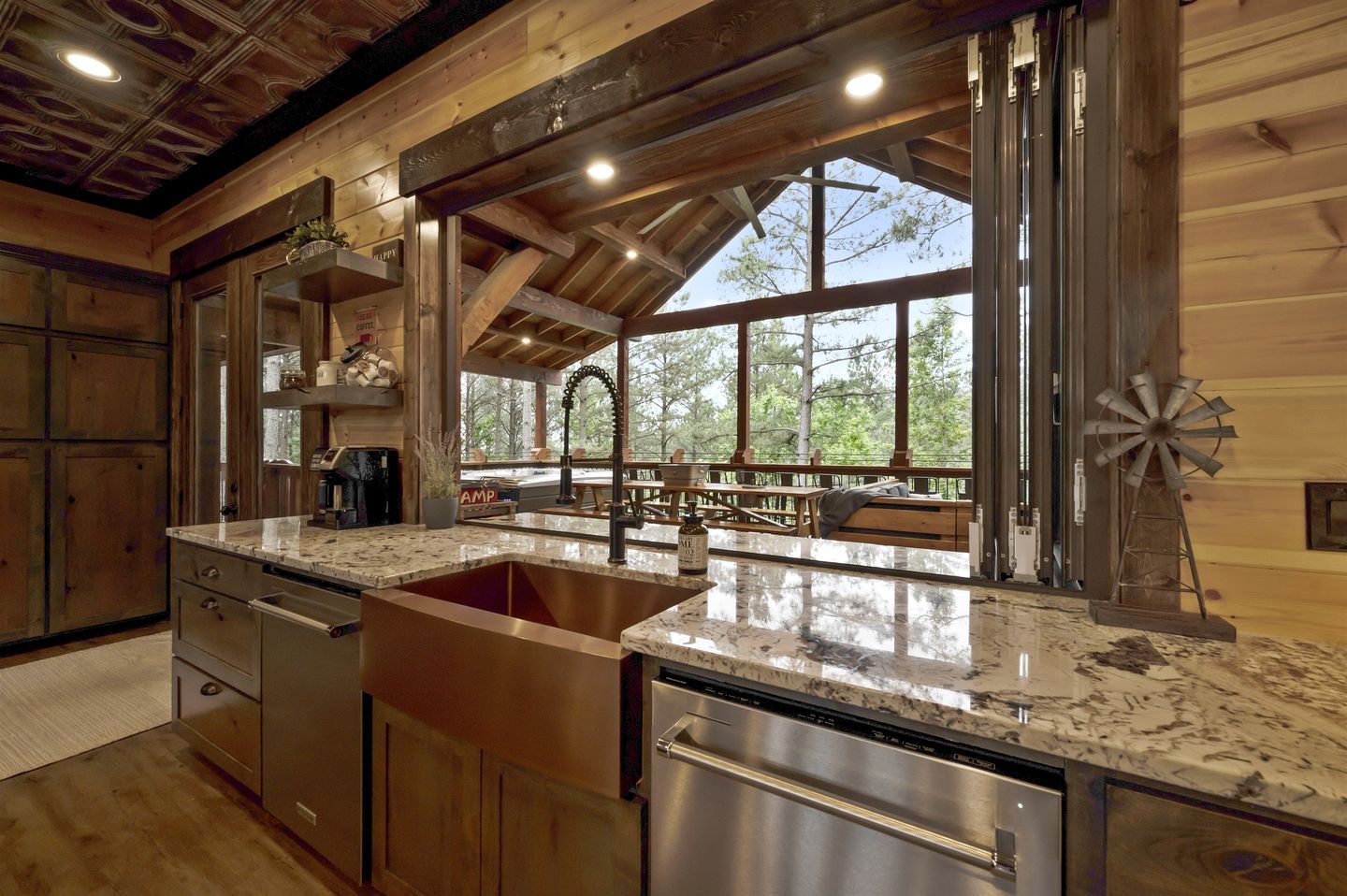Una cocina con pileta de acero inoxidable, muebles de madera y un ventanal con vistas a una terraza.