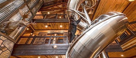 Un interior rústico con vigas de madera, una gran estructura espiral metálica y ciervos disecados.