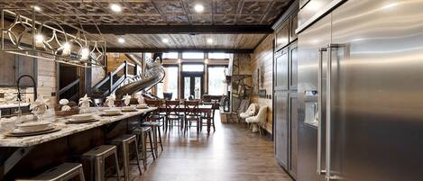 A kitchen with a stainless steel refrigerator, wooden flooring, and a central island with stools.