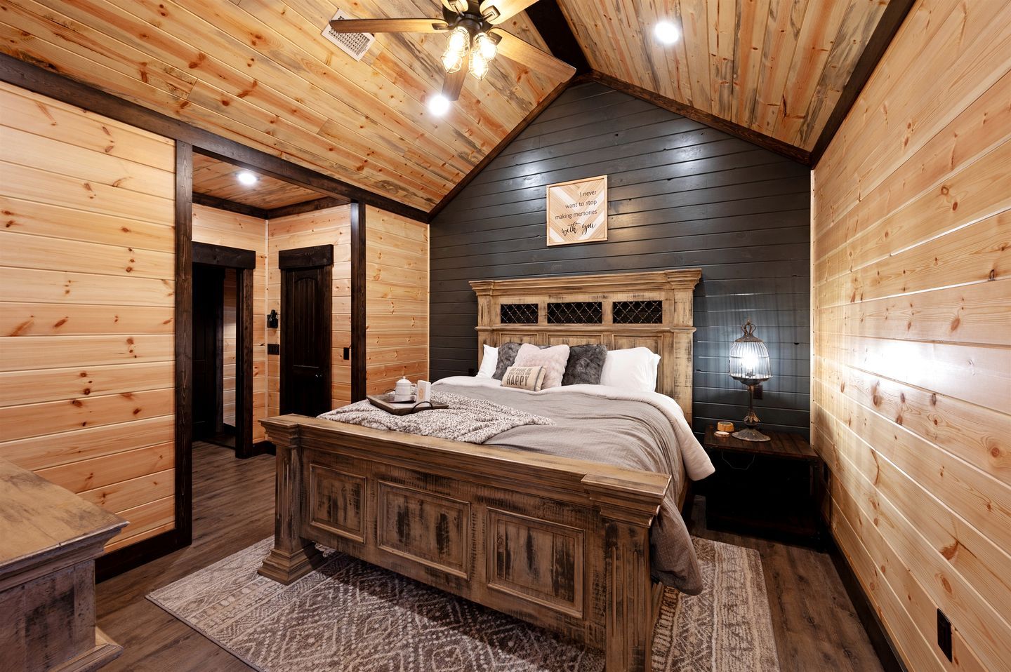 A wooden-paneled bedroom with a large bed, a ceiling fan, and a nightstand with a lamp.