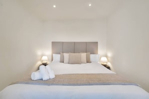 Ein Hotelzimmer mit einem großen Bett, zwei Nachttischen mit Lampen und einem Kopfteil.