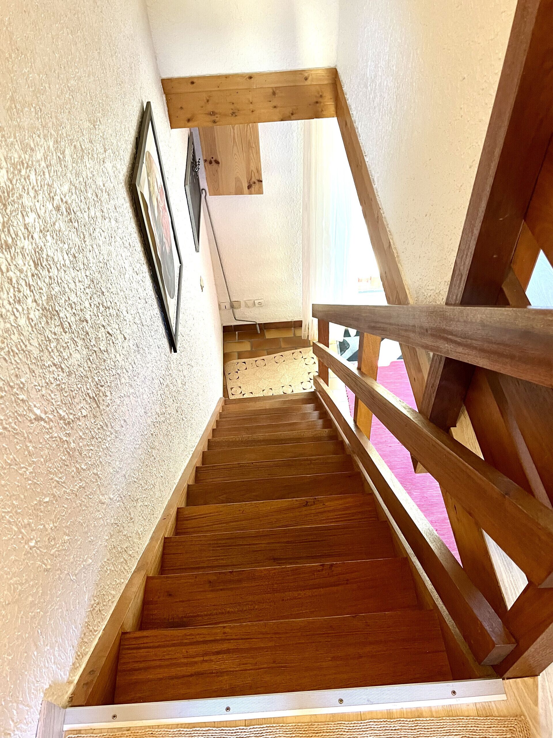 A wooden staircase with a handrail, a framed picture on the wall, and a window with a view.