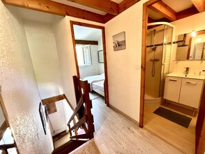 Eine Treppe führt zu einem Schlafzimmer mit Holzboden, einem Badezimmer mit Dusche und einem kleinen Bild an der Wand.