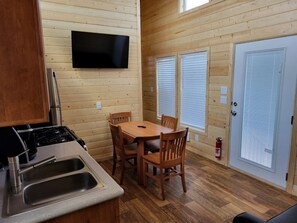 A wooden interior with a kitchen, dining table, chairs, a television, and a door with a window. - Modern Tiny Home Retreat with Stunning Stargazing Views in Williams, Arizona (Williams)