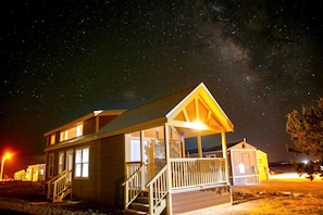 A small, two-story wooden building with a porch and a staircase, under a starry night sky. - Modern Tiny Home Retreat with Stunning Stargazing Views in Williams, Arizona (Williams)
