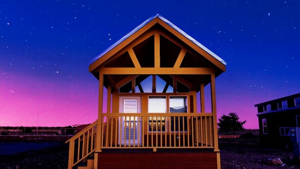 Uma cabana de madeira com varanda, escada e vista para o céu noturno.