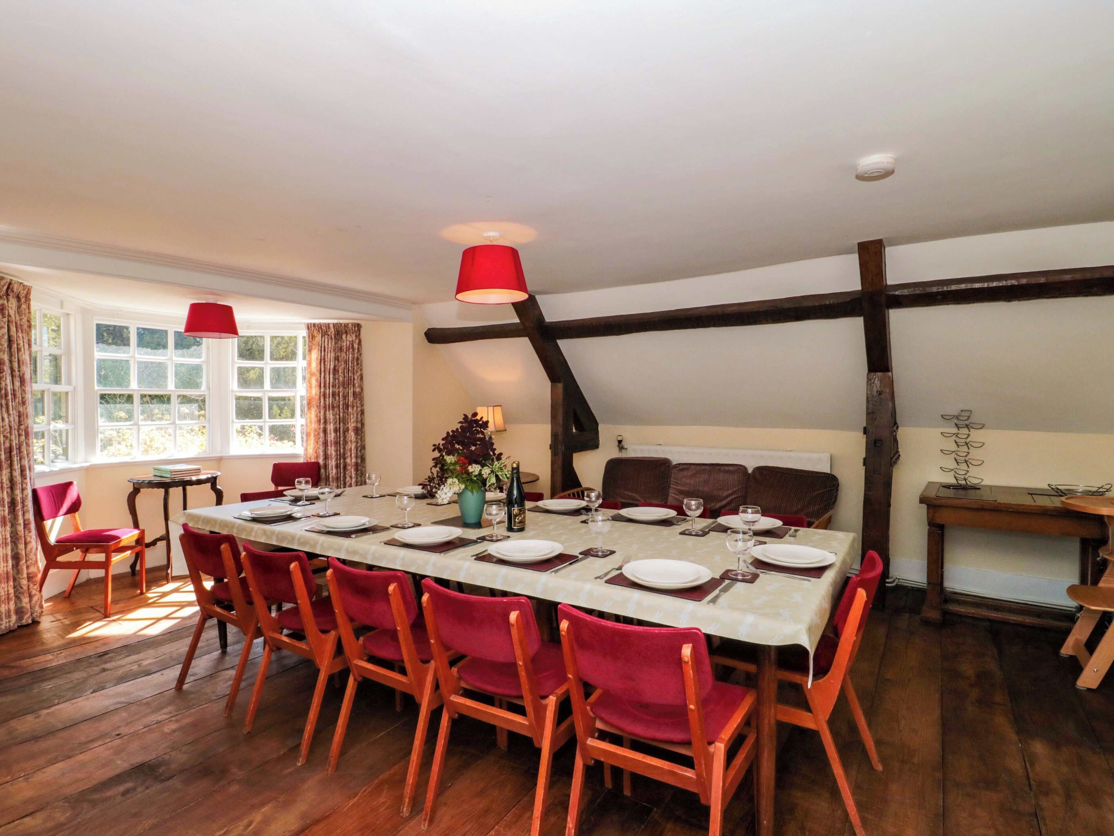 A dining room with a long table, red chairs, and a vase of flowers.
