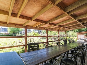 A covered outdoor dining area with a wooden table and chairs, surrounded by a wooden fence and greenery. - The West Wing (Gloucester)