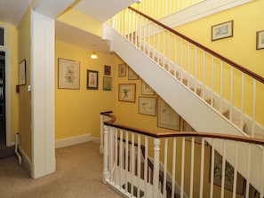 A staircase with white railings and wooden handrails, leading to a landing with framed botanical prints on the wall. - The West Wing (Gloucester)