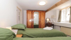 A bedroom with two beds, a wooden wardrobe, a desk with a chair, a mirror, and a window with curtains. - The West Wing (Gloucester)