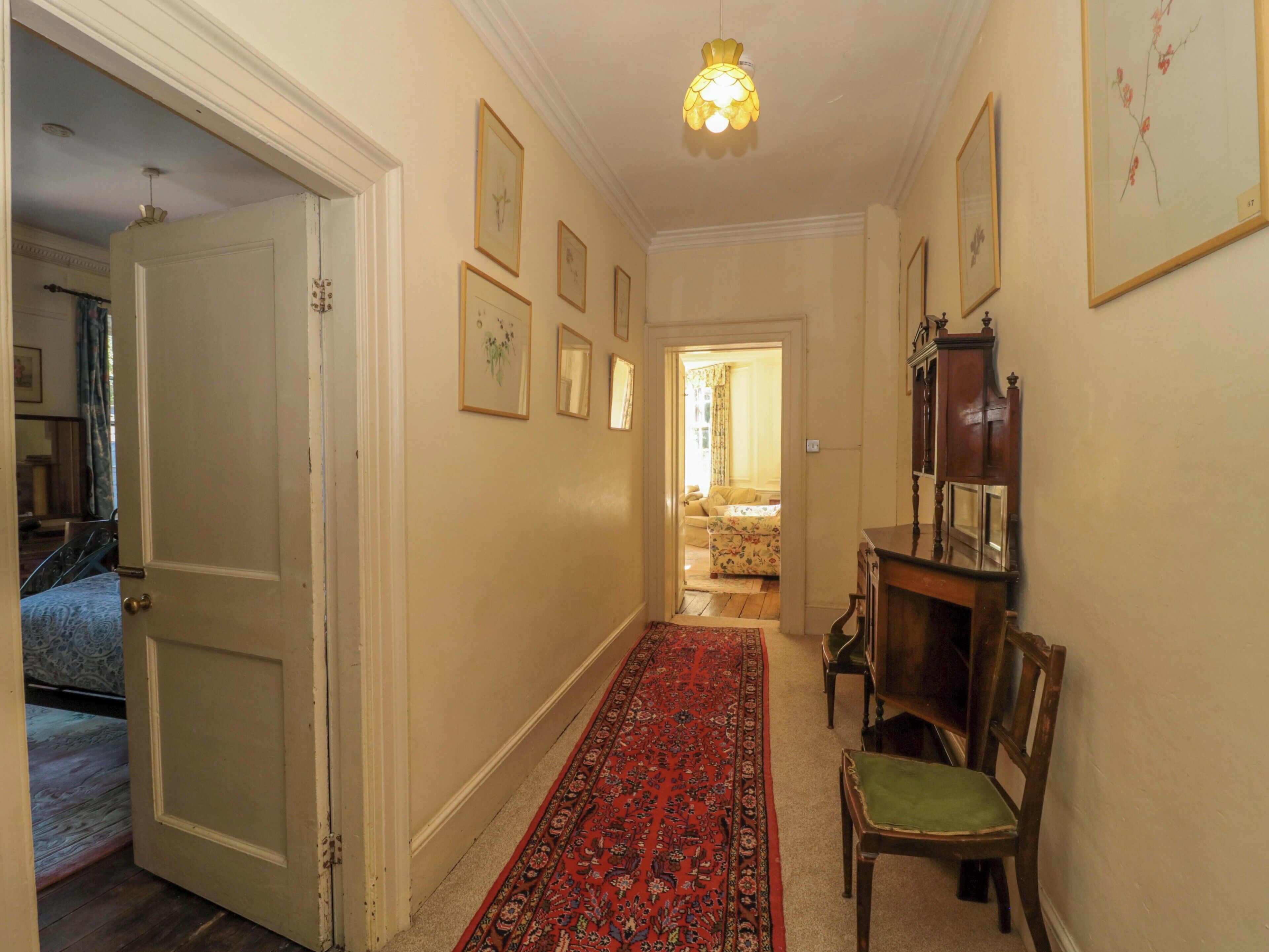 A hallway with a red carpet, wooden furniture, and framed artwork on the walls.