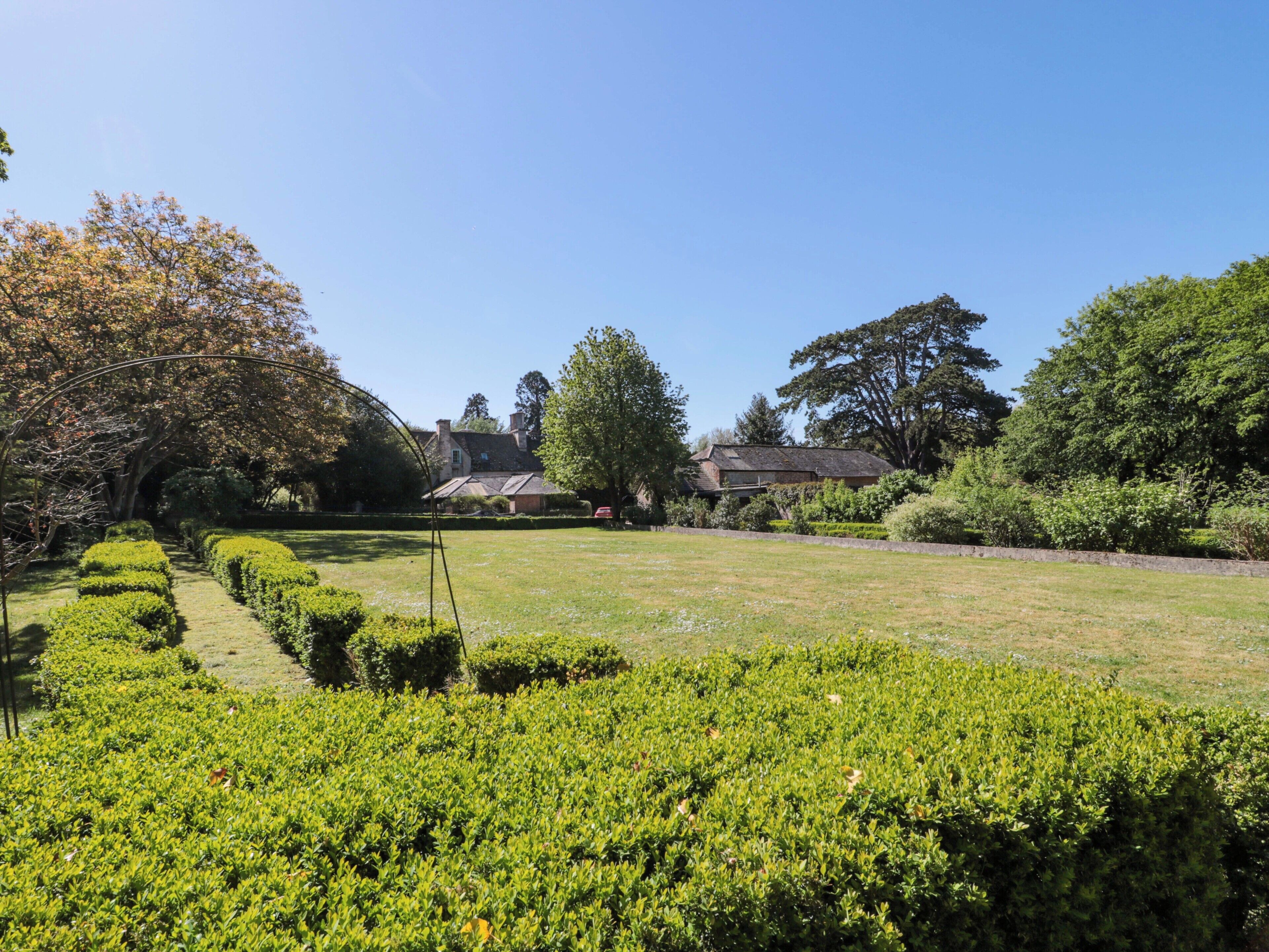 Un jardin avec des haies soigneusement taillées, un sentier et un bâtiment doté d’un toit en pente.