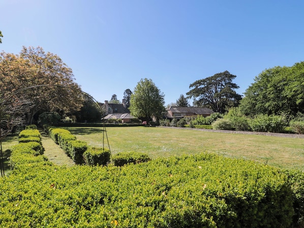 A garden with neatly trimmed hedges, a pathway, and a building with a sloped roof. - The West Wing (Gloucester)