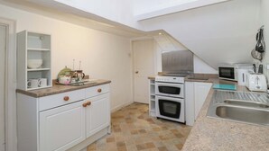 A compact kitchen with white cabinetry, a built-in oven, a microwave, and a sink. - The West Wing (Gloucester)