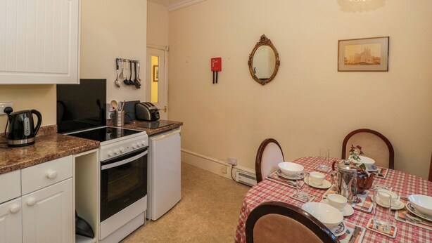 A compact kitchen with a stove, oven, and a dining area with a table set for two. - The West Wing (Gloucester)