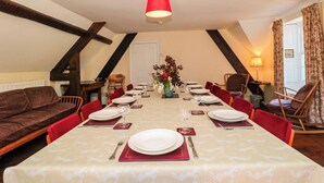 A dining room with a long table set for six, red chairs, a vase with flowers, and a red lamp. - The West Wing (Gloucester)