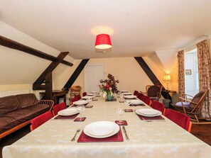 A dining room with a long table set for six, red chairs, a vase with flowers, and a red lamp. - The West Wing (Gloucester)