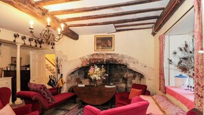 A traditional room with a stone fireplace, red upholstered chairs, a patterned rug, and a chandelier. - The West Wing (Gloucester)