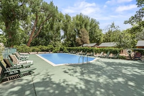 Ein rechteckiger Pool, umgeben von grünen Liegestühlen und einer gepflasterten Liegefläche.
