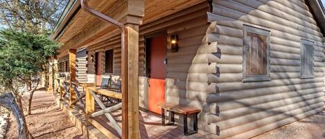 A log cabin with a porch, a bench, and a door.
