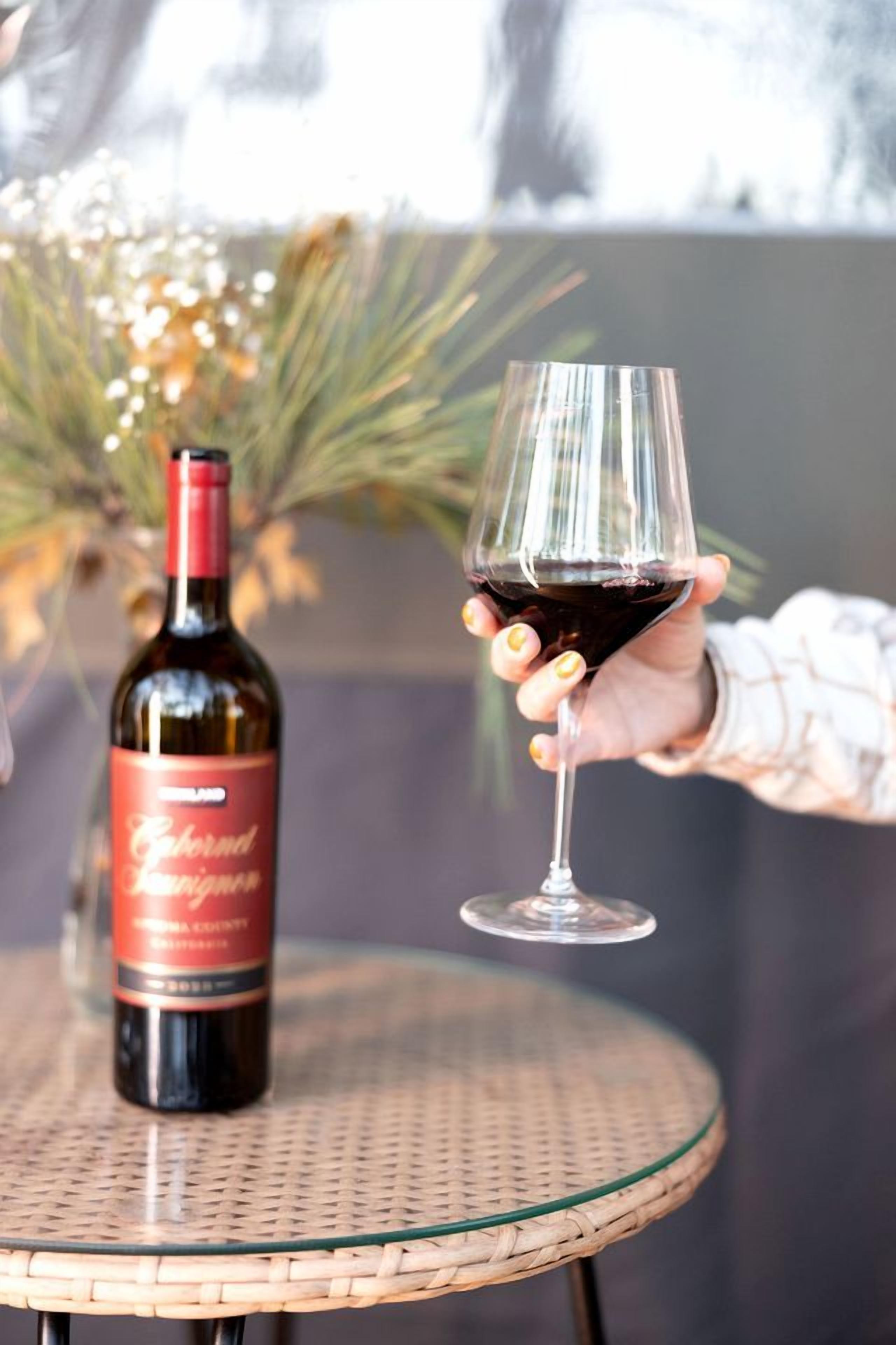 Una botella de vino y una copa de vino tinto sobre una mesa redonda de vidrio con un borde tejido.