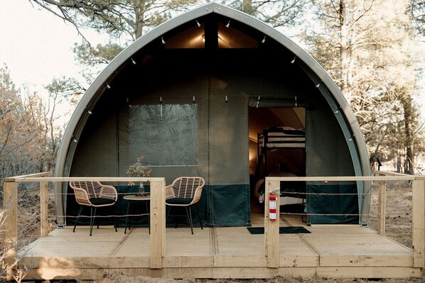 A dome-shaped tent with a wooden deck and two wicker chairs.