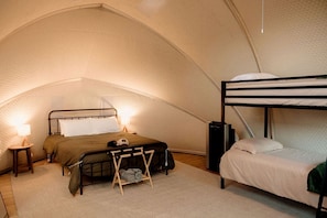 A tented accommodation with a bunk bed, a single bed, a small table with a lamp, and a speaker.