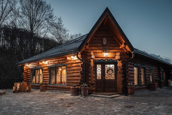 Une cabane en rondins avec une entrée pavée de pierres, de grandes fenêtres et une porte décorative.