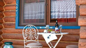 Eine Holzhütte mit einer steingepflasterten Veranda, einem Tisch mit Stühlen, einer Weinflasche und einem dekorativen Fensterrahmen.