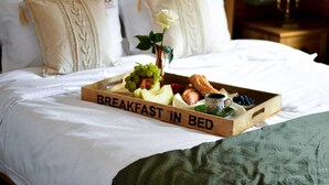 Ein Bett mit Tablett, beschriftet mit 'BREAKFAST IN BED', mit Früchten, Gebäck und einer Tasse.