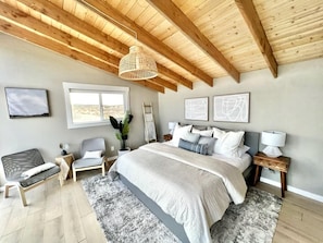 A bedroom with a large bed, a wooden ceiling, a window, and a bedside table with a lamp.